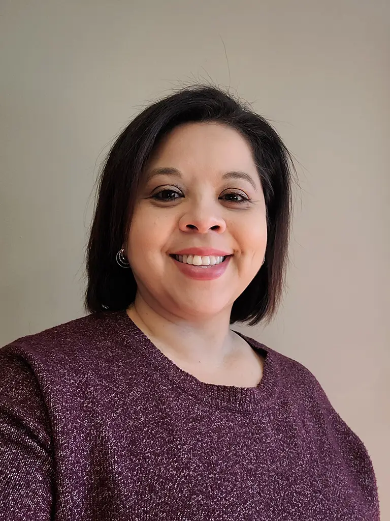 A woman with straight, dark hair and wearing a maroon sweater smiles at the camera against a plain beige background.