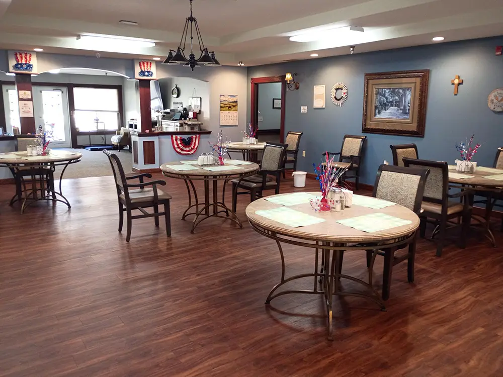 HorizonClare-3 A dining area with round tables and chairs, wooden flooring, patriotic decorations, and a counter in the background. Each table has small centerpieces and place mats.