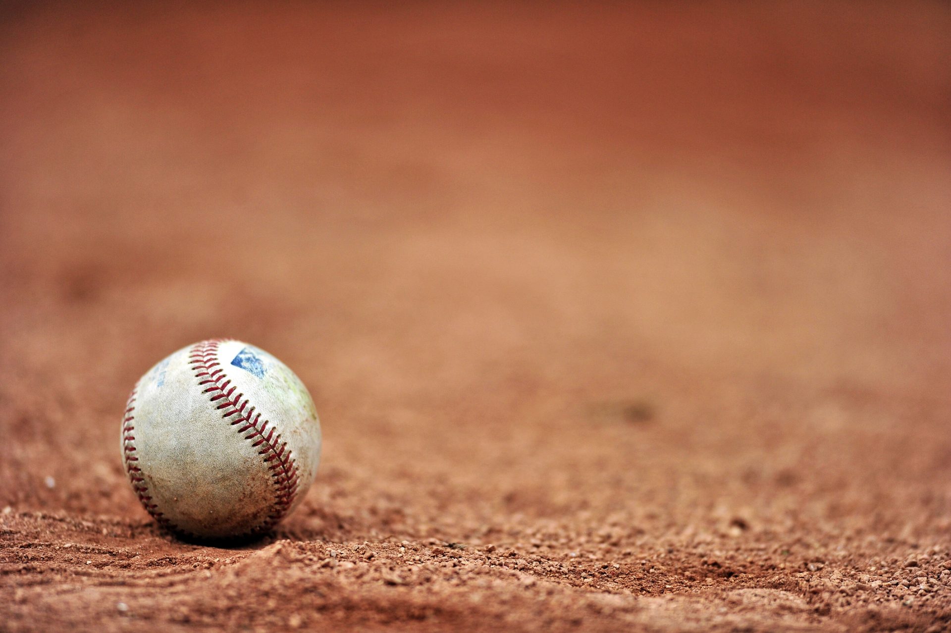 A baseball resting on a dirt field with a blurred background, capturing the spirit of Heaven & Home, as seen through the lens of Jeff Pettinga.