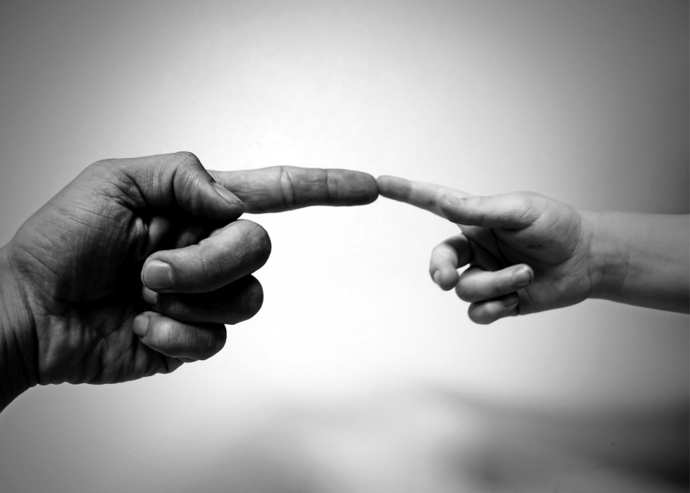 A close-up of an adult hand and a child's hand reaching towards each other, their index fingers almost touching—a tender moment reflecting the Image of God in everyday Christian living against a plain background.