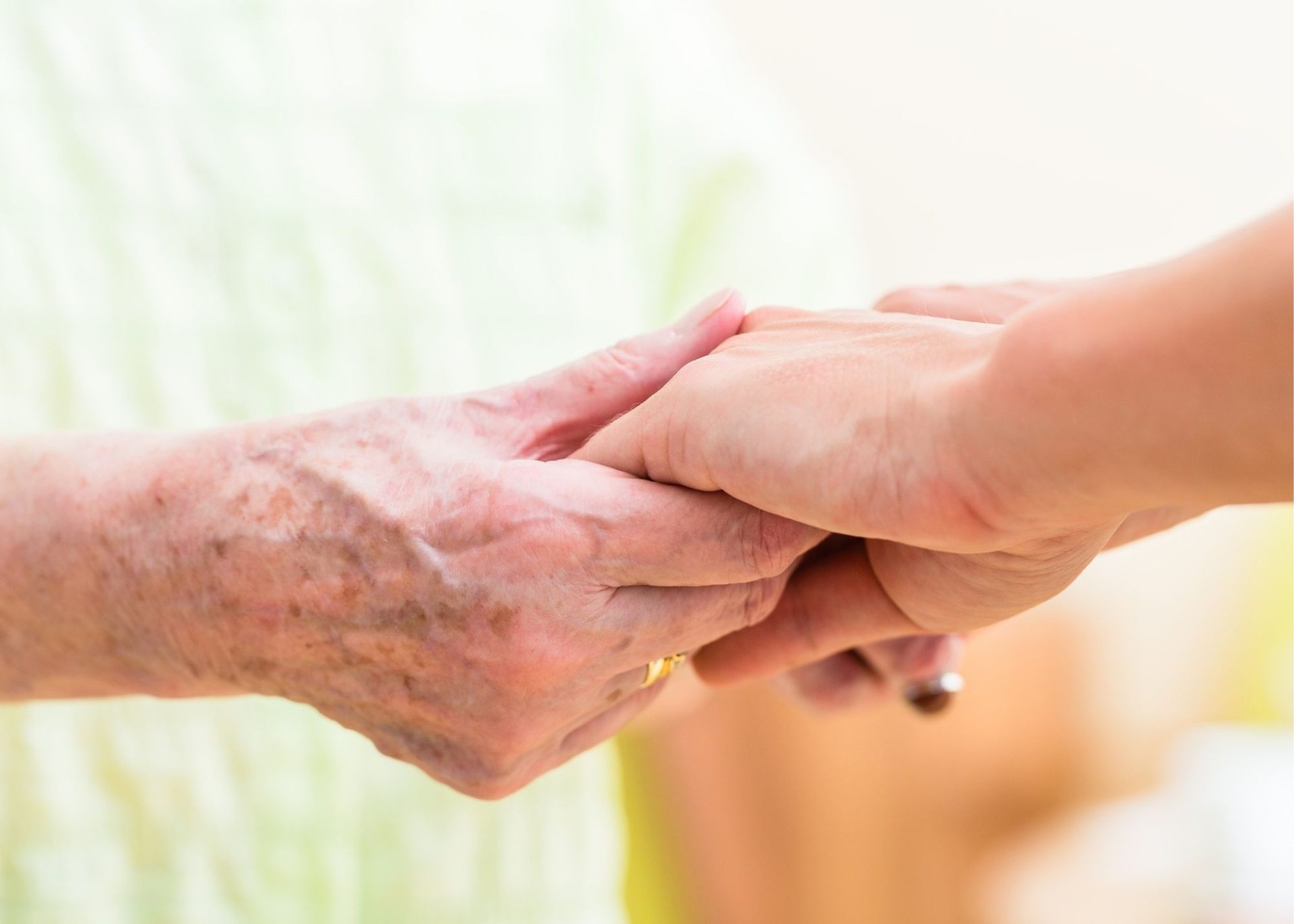 A younger person gently holds the hands of an older person with visible age spots, symbolizing care and support—a heartwarming moment captured for our Volunteer Newsletter, Spring 2022.