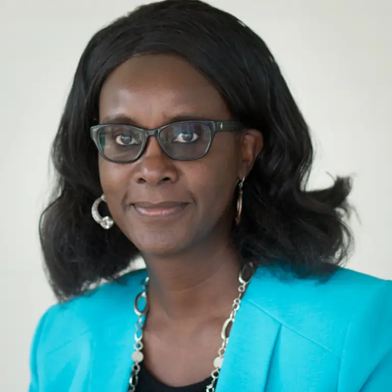 A woman wearing glasses and a turquoise blazer, with shoulder-length black hair, facing the camera against a plain background.