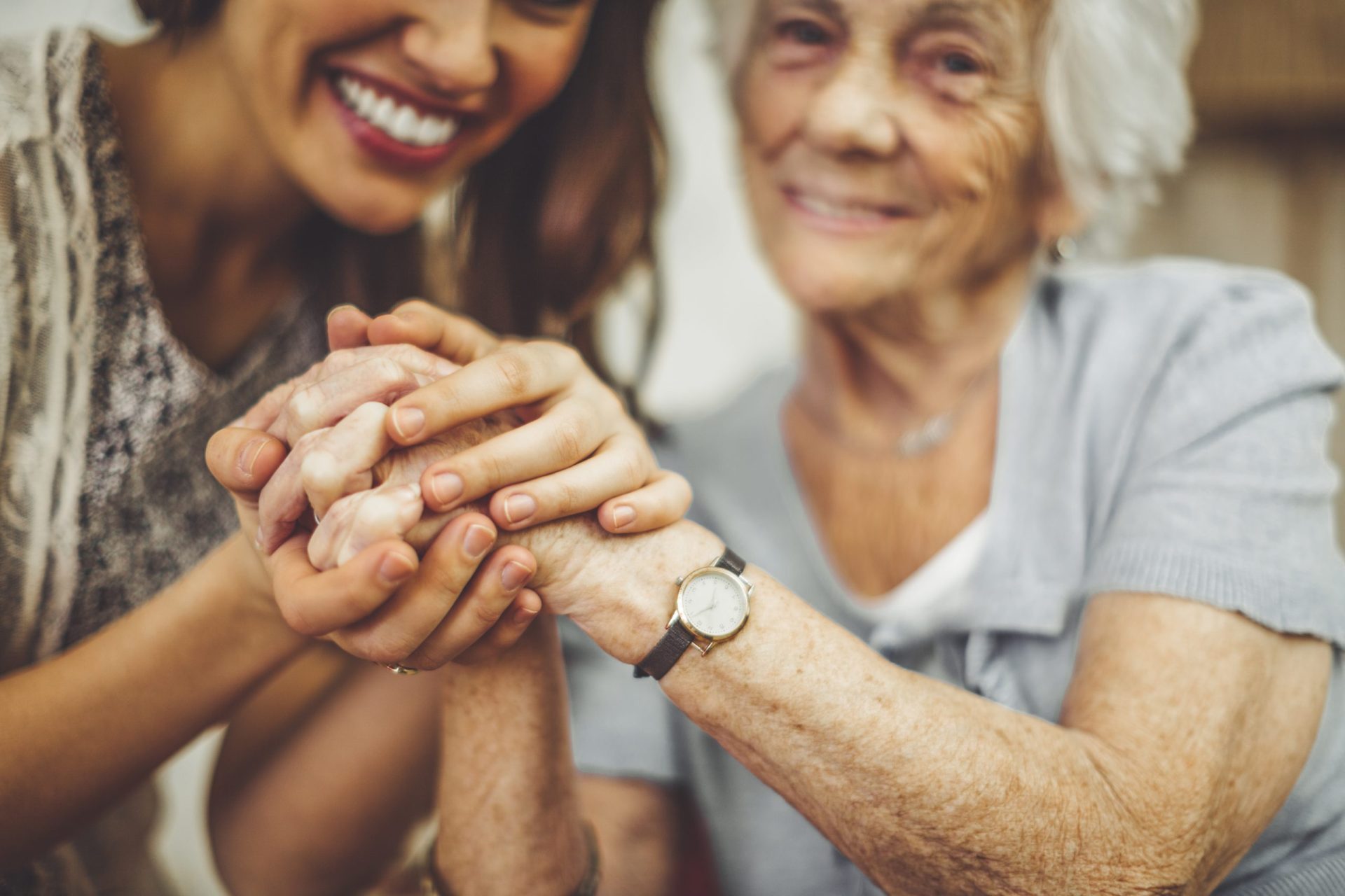 A younger woman and an older woman smile while holding hands closely, showing affection and connection, reflecting the warmth often found in quality assisted living.