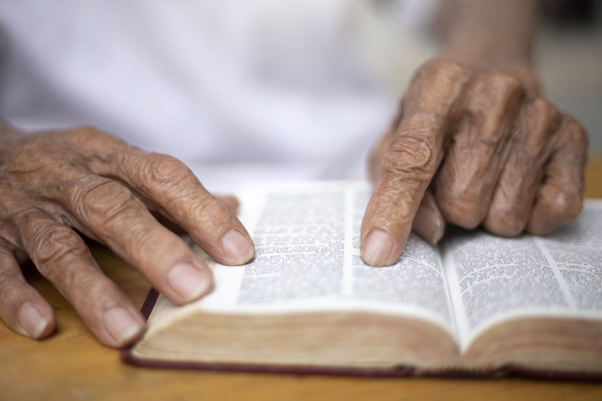 Close-up of an elderly person's hands holding an open book, with one finger pointing to the text about Baruch in the Bible.