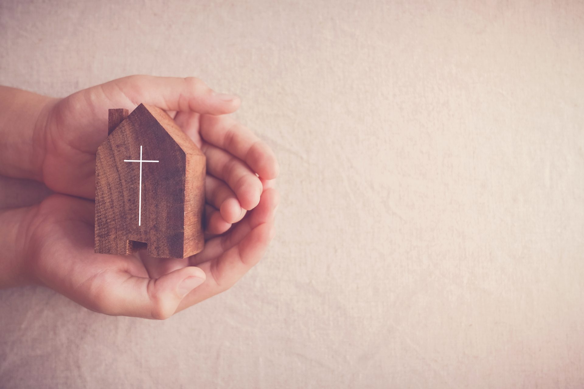 Hands gently holding a small wooden house with a white cross symbol on it, set against a light background—perfect imagery for a Spiritual Care Blog inspired by the Great Commandment.