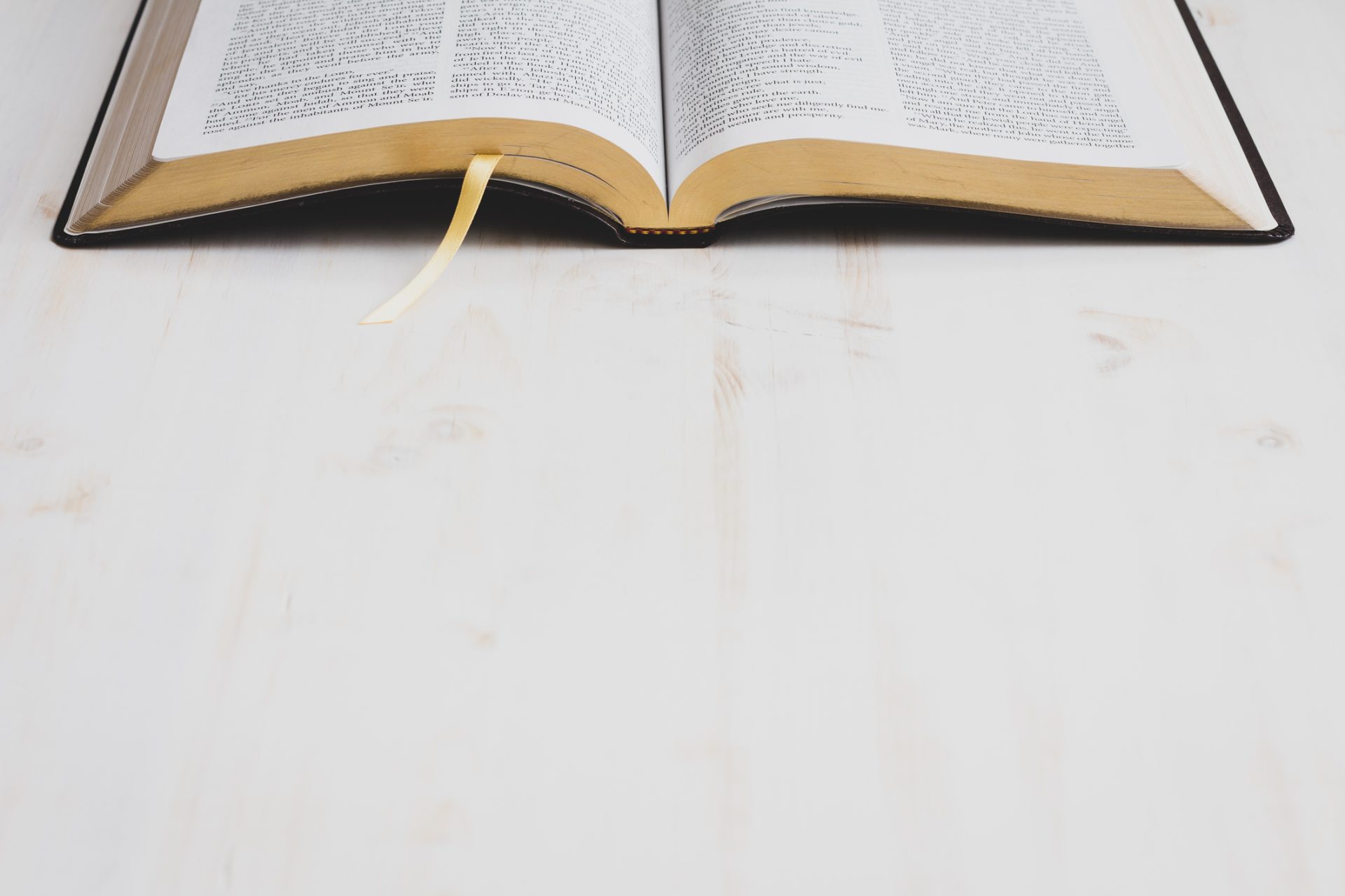 An open book with a yellow ribbon bookmark lies on a light wooden surface, its pages filled with text about standing on the promises of God, offering insights into spiritual care.