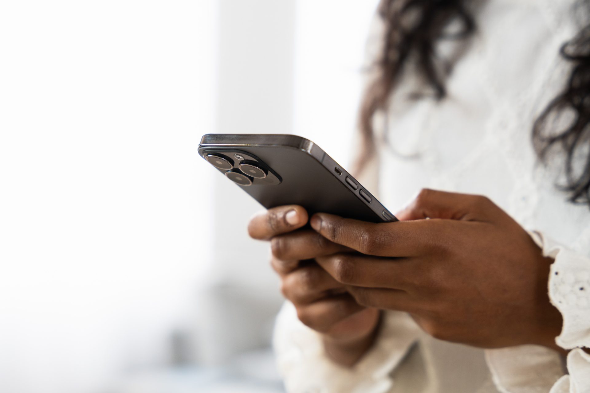 A person wearing a white long-sleeve top holds and uses a smartphone with both hands, perhaps reflecting on Spiritual Care or reading the latest February Blog from God Calling.