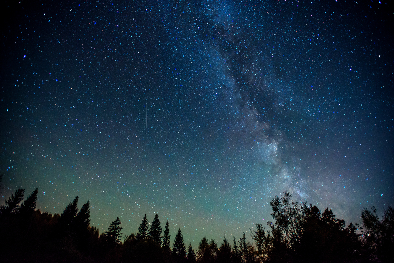 Night sky filled with stars and the Milky Way galaxy visible above a silhouette of trees on the horizon, a peaceful reminder of God's Goodness under the vast heavens.