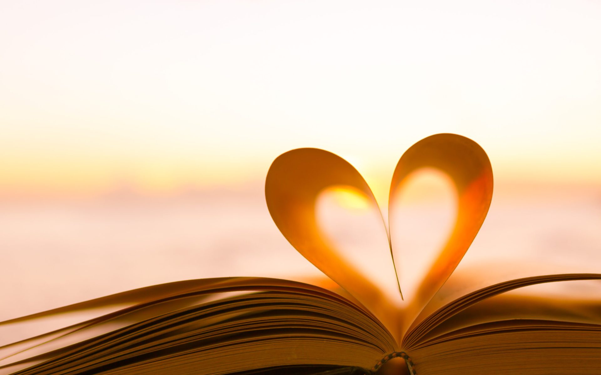 An open book with pages curved to form a heart shape, set against a warm, blurred sunset background—perfect for illustrating God's love or spiritual care on your spiritual blog.
