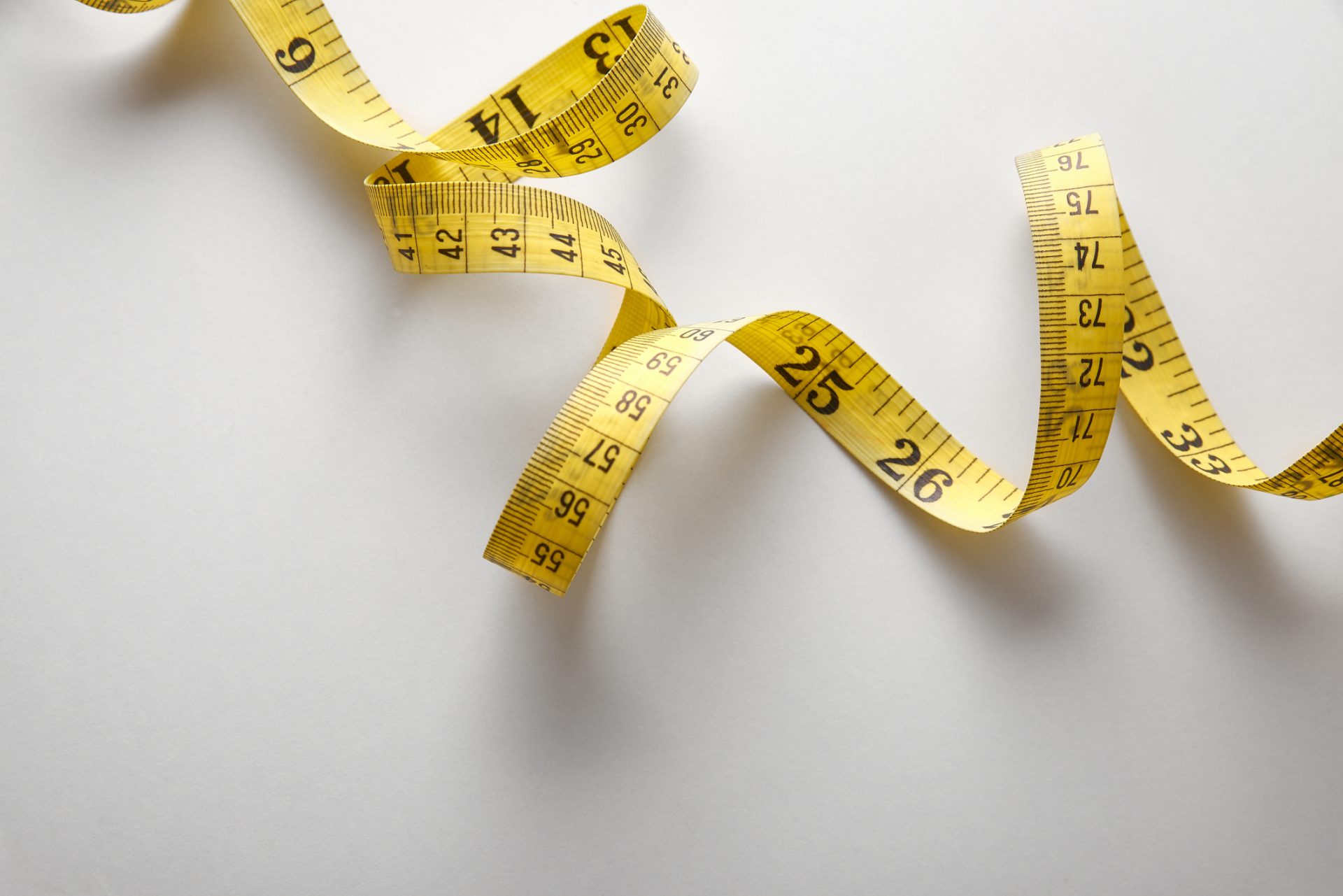 A yellow measuring tape with black markings is loosely curled on a plain white surface, subtly reminding us of how spiritual care measures the depth of God’s love in everyday moments.