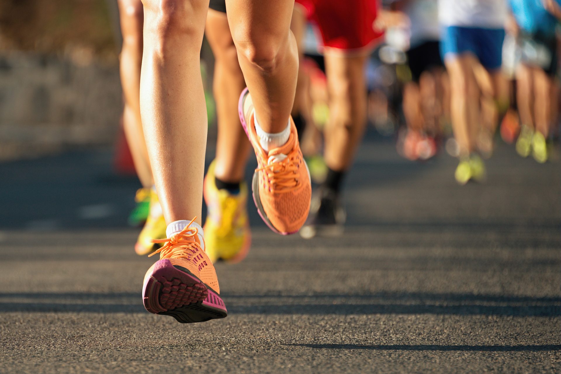 Close-up of runners' legs and feet in colorful athletic shoes on a paved road during a race, highlighting movement and activity—an inspiring moment to "Press On," perfect for a blog post about perseverance or spiritual care.